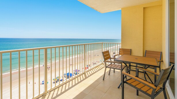 A balcony with a view of the beach, a table with chairs, and a railing. - Oceanfront-EV Charging-Aruba #704 (Daytona Beach Shores)