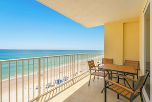 Een balkon met uitzicht op het strand, een tafel met stoelen en een hekwerk.