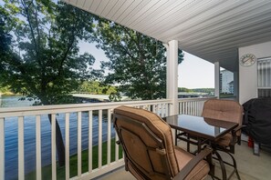 Enjoy a waterfront view from this balcony with a table and chairs, perfect for outdoor dining. A barbecue grill and clock add to the convenience.