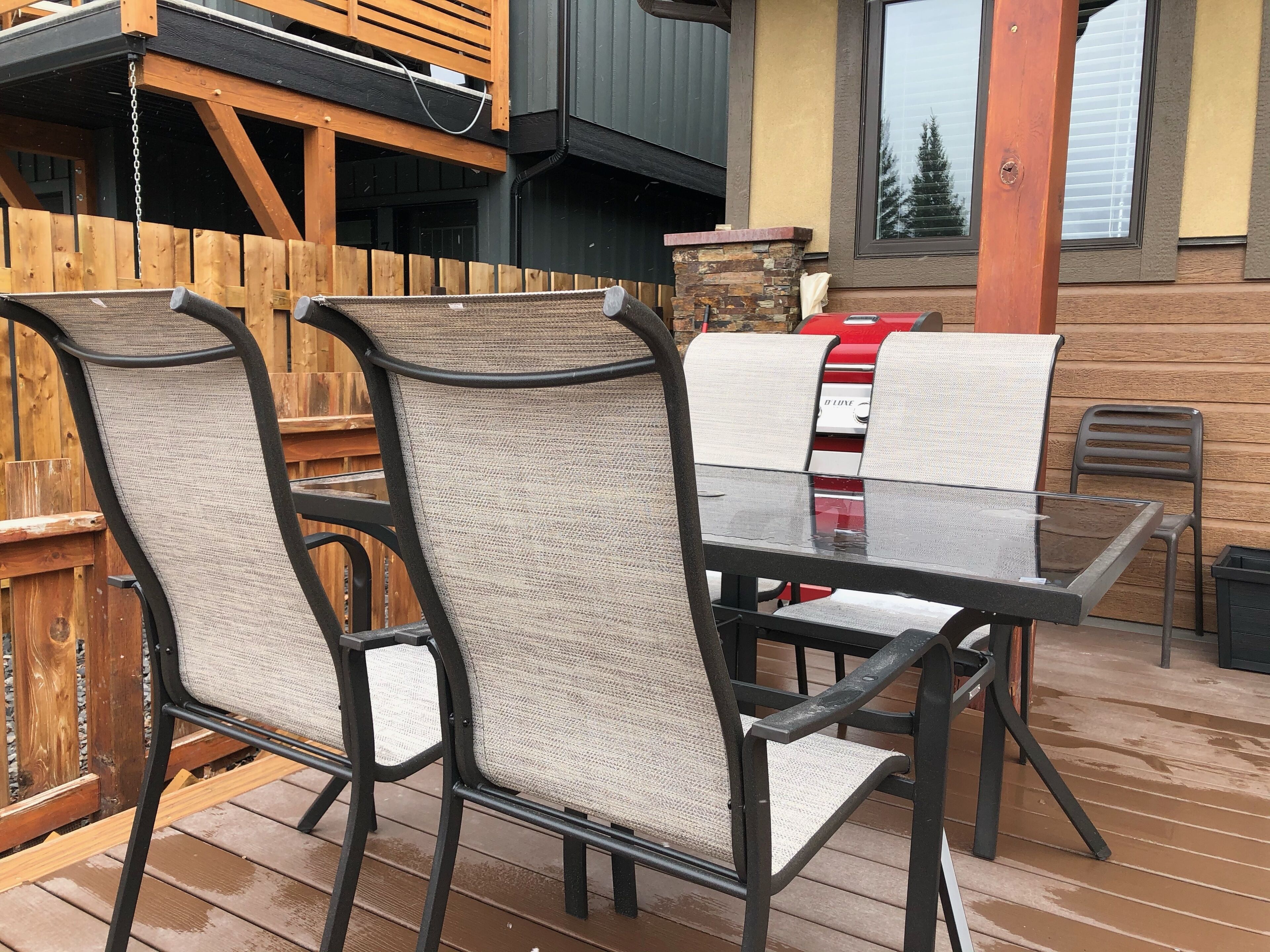 Eine Holzterrasse mit einem Tisch aus Glas und vier Stühlen mit Netzrücklehnen.