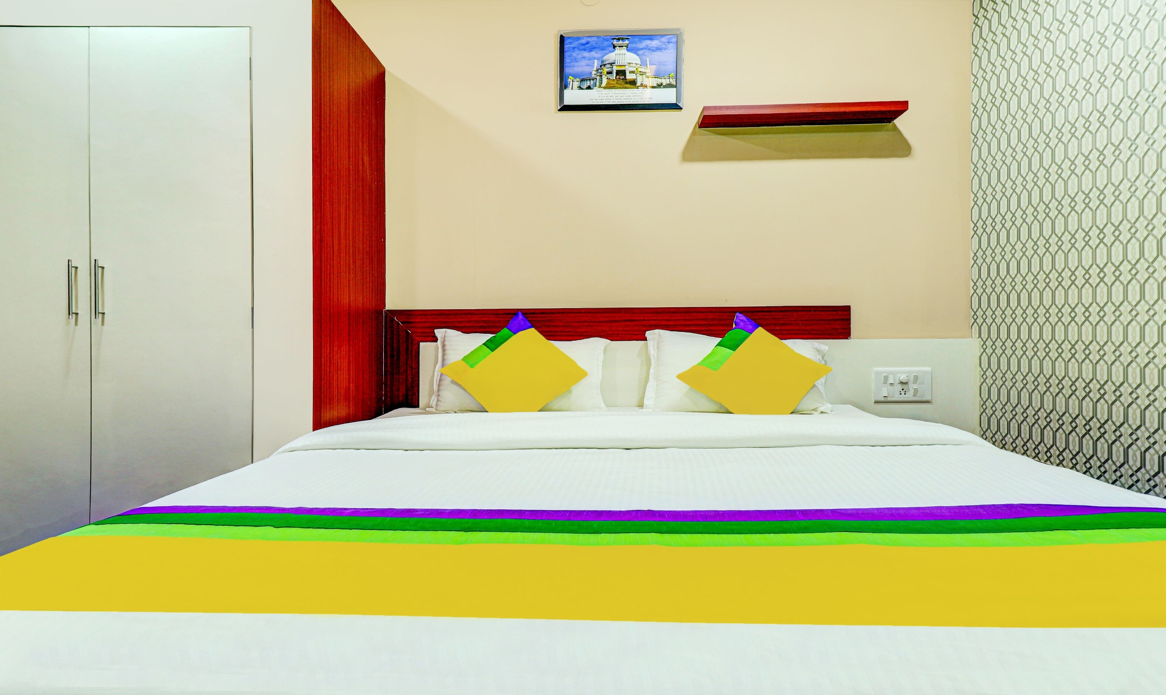 Quarto de hotel com cama, guarda-roupa, um quadro na parede e um padrão no papel de parede.