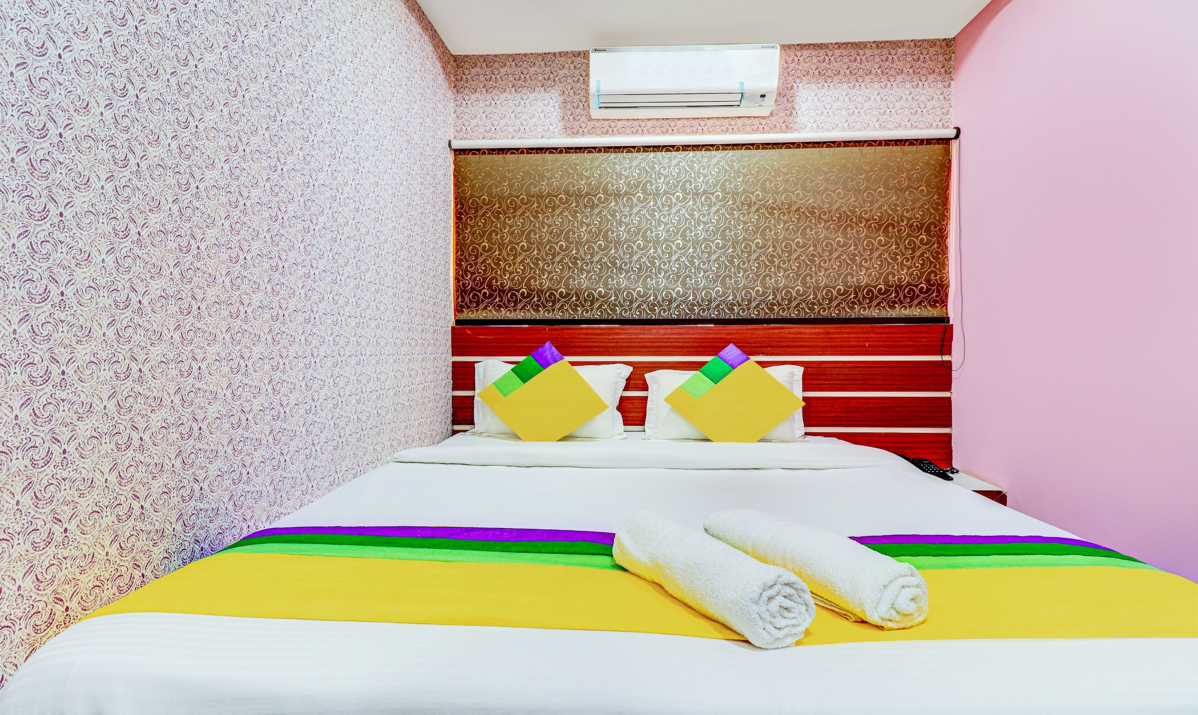 A hotel room with a patterned wallpaper, a red-striped headboard, and a bed with a striped bedspread and pillows.