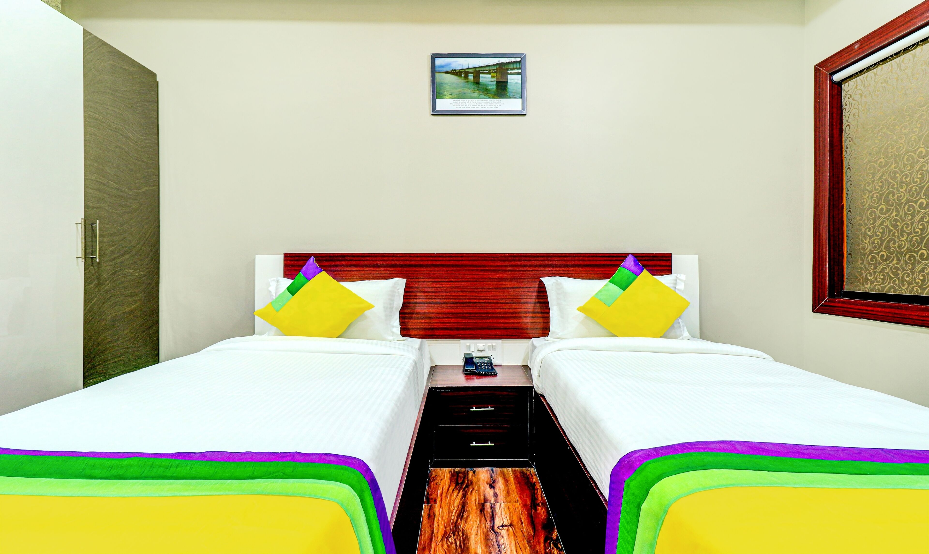 A hotel room with two beds, a wooden floor, a red headboard, and a framed picture on the wall.