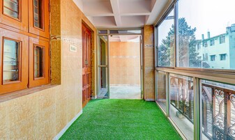 Un pasillo con piso verde artificial, puertas de madera y barandilla de cristal que da a un edificio.