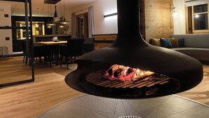 A modern kitchen with a central wood-burning stove, a dining area with chairs, and a wooden wall.