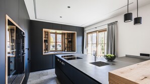 A modern kitchen with a central island, dark cabinetry, and a large window with curtains.