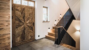 A wooden door with a geometric pattern, a staircase with wooden steps and black railings, and a small window with a vase of flowers.