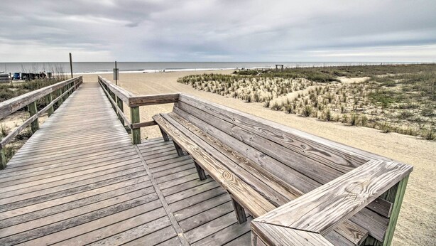 Een houten looppad naar een zandstrand met duinen en een bewolkte lucht.