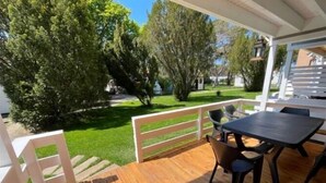 Um deck de madeira com mesa e cadeiras, cercado por grades brancas e gramado verde.