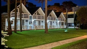 Uma fileira de cabanas brancas e modernas com telhados inclinados, rodeadas por árvores e um gramado bem cuidado.
