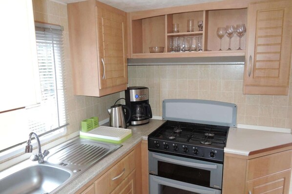 A kitchen with wooden cabinets, a gas stove, a coffee maker, and a sink.