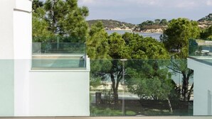 A modern building with a glass balcony overlooking a coastal landscape with trees and a body of water. - Villas Acrotel Porto Brava, Ormos Panagias (Ormos Panagias)