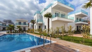 A modern pool area with a rectangular pool, surrounded by wooden decking and glass balustrades. - Villas Acrotel Porto Brava, Ormos Panagias (Ormos Panagias)