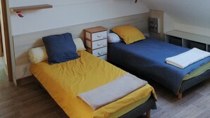 Une chambre avec deux lits, un ventilateur de plafond, une lucarne et une petite table de chevet.