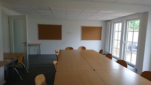 Un salón de conferencias con una mesa larga, sillas, una puerta y dos paneles de anuncios.