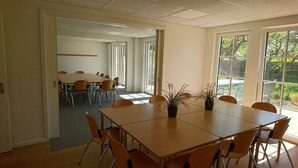Un salón de conferencias con una gran mesa y sillas, ventanas amplias con vistas a zonas verdes y una puerta que da a otra habitación.