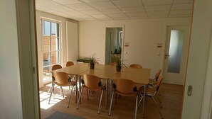 Un salón de conferencias con una mesa rectangular, seis sillas y dos plantas en macetas.