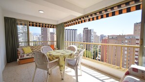 A balcony with a table and chairs, a sofa, and a view of city buildings. - LAS ADELFAS (2 BEDROOM) (Benidorm)