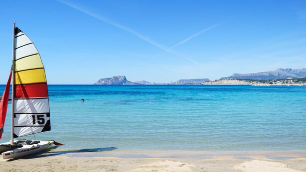 Una playa con un velero y un cielo azul despejado.