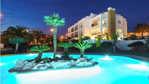 Un hotel moderno con zona de piscina, palmeras y rocas.