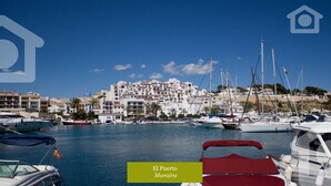 Un pueblo costero con edificios blancos, un puerto deportivo con barcos y palmeras.