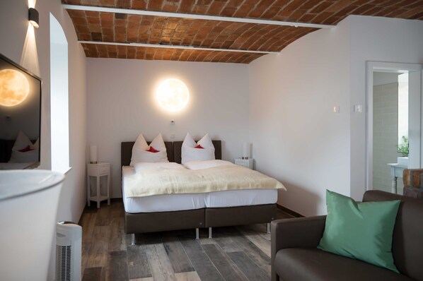 A bedroom with a bed, bedside tables, a mirror, a green pillow, and a brick ceiling.