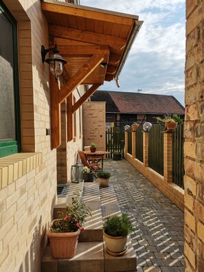 Un patio couvert avec un mur en briques, une pergola en bois, des sièges d’extérieur et des plantes en pot.