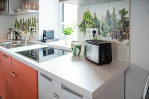 Una cuina moderna amb fogó d'inducció integrat, torradora, bullidor i una planta en test.