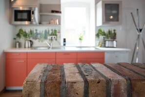 Une cuisine avec un plan de travail en briques, des placards rouges et un four à micro-ondes.