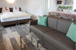 A modern hotel room with a bed, a sofa, a glass coffee table, and a kitchen area with a microwave.