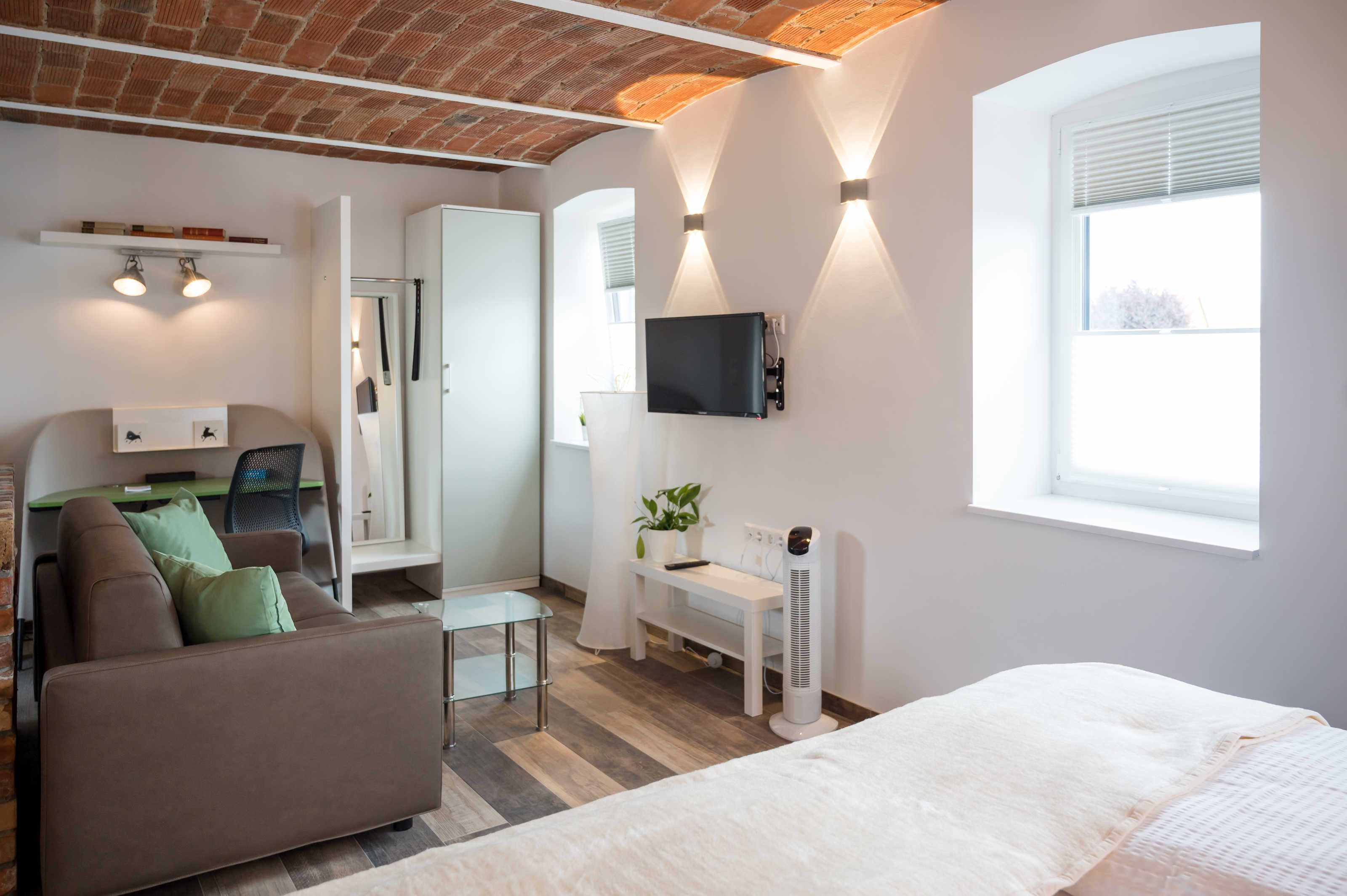 A modern room with a bed, a sofa, a desk, a TV, and a window.