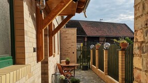 Een overdekt terras met een bakstenen muur, een houten pergola, buitenmeubels en potplanten.