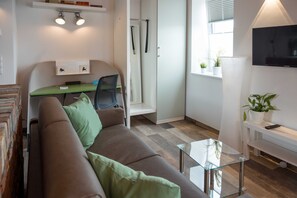 Un espace de vie compact comprenant un canapé, une petite table, un téléviseur fixé au mur et une porte dotée d’un porte-serviettes.