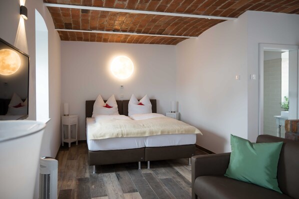 Een slaapkamer met een bed, nachtkastjes, een spiegel, een groen kussen en een bakstenen plafond.