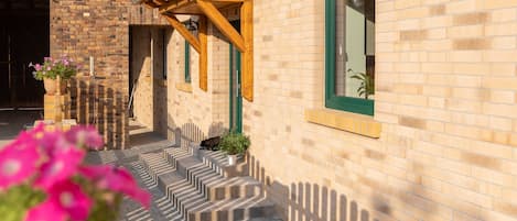 A building with a brick exterior, wooden steps, and green-framed windows.