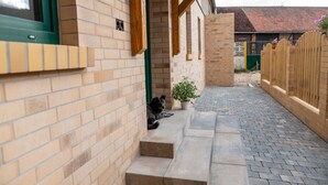 Een bakstenen gebouw met een hond die op de treden uitrust, een bloempot en een houten omheining.