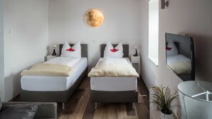A modern hotel room with two beds, a round wall decoration, a mirror, and a small table.