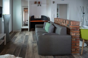 Un salon moderne avec un canapé gris, un mur d’accent en briques, un bureau et un grand vase gris.