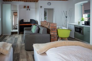 A modern room with a bed, a sofa, a desk, and a kitchen area.