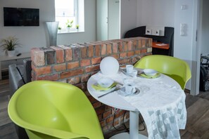 Een eethoek met een steen scheidingswand, een ronde tafel met een witte tafelkleed en twee felgroene stoelen.