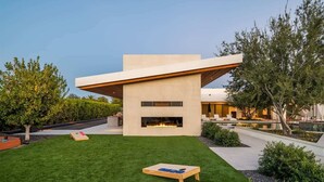 A modern house with a flat roof, a central fireplace, and a well-maintained lawn.