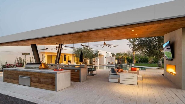 A modern outdoor living area with a pool, seating, and a TV screen.