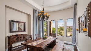 A dining area with a wooden table, benches, a chandelier, and a view through large windows. - Dreamy Desert Oasis with Game Room, Heated* Pool! (Scottsdale)