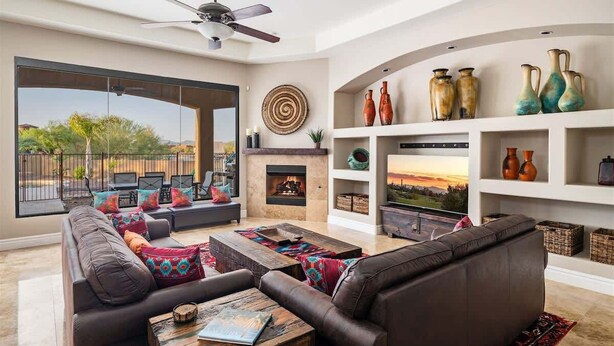 A modern living room with a fireplace, leather sofas, and a view of the outdoors. - Dreamy Desert Oasis with Game Room, Heated* Pool! (Scottsdale)