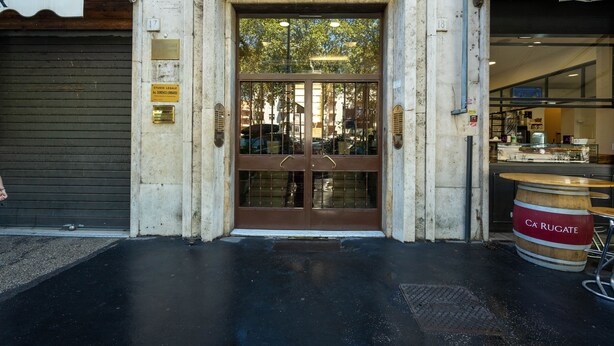 Une entrée d’immeuble avec une porte à deux battants, une enseigne indiquant qu’il s’agit d’un cabinet d’avocats, et un tonneau en bois à l’extérieur.