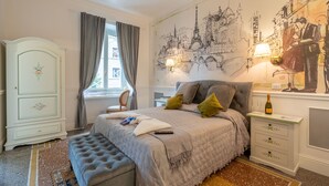 Une chambre à coucher comprenant un lit, une table de chevet, une commode, un banc et une fresque représentant Paris.