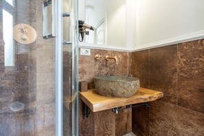 A bathroom with a stone sink, a hairdryer, and a mirror. - Capital Rooms (Rome)