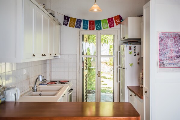A kitchen with white cabinets, a wooden countertop, a hanging decorative banner, and a refrigerator with magnets. - Sunny Beachfront Home (Mola Kalyva, Halkidiki)