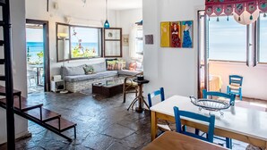 Un salon chaleureux avec un canapé, une table à manger et des chaises. Les fenêtres offrent une vue sur l’océan.