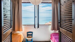 Une pièce avec une grande fenêtre, une chaise, un lit et un luminaire suspendu.